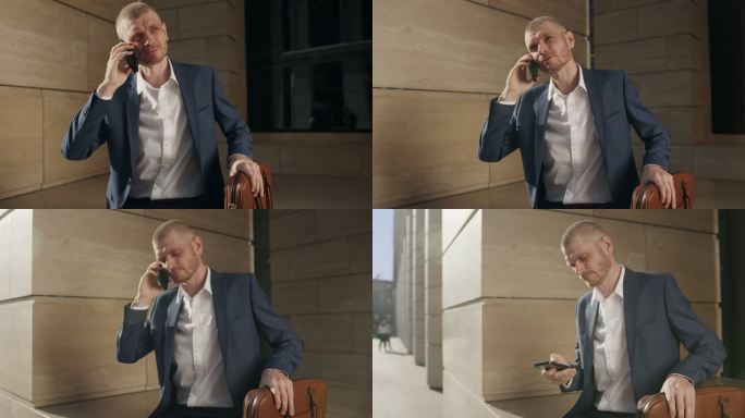 一位年轻迷人的金发商人坐在现代建筑立面的石头上，手里拿着棕色皮革笔记本电脑，用智能手机完成了对话