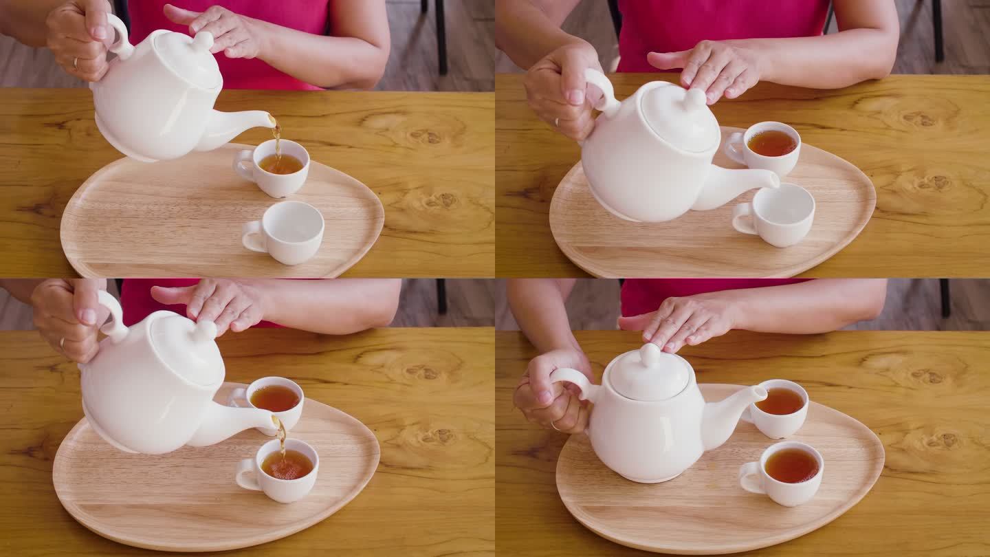 在家里，女人把茶壶里的茶倒进木桌上的茶杯里，茶道概念