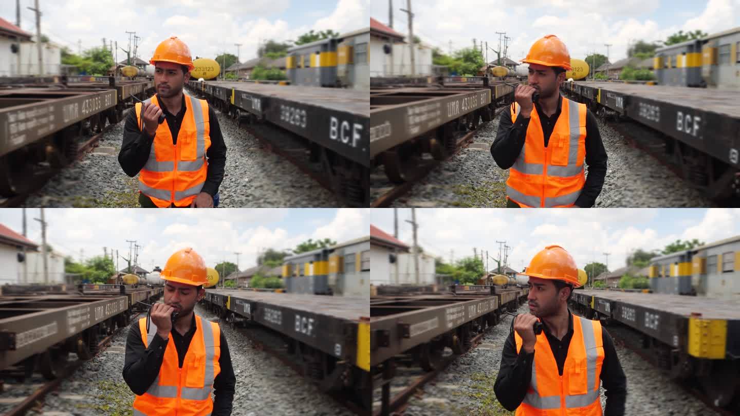 亚洲工程人员戴着头盔和制服在火车站上检查火车。男工程专家使用步行对讲机检查货运列车。