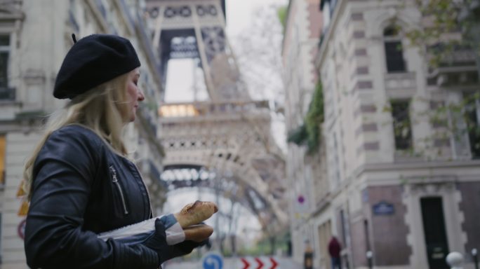 SLO MO时尚的法国女人在埃菲尔铁塔边走边吃法棍面包