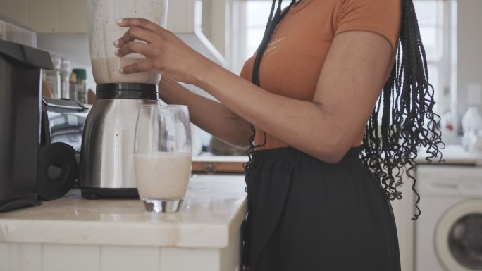 一位女士在厨房检查手机时喝了一杯蛋白奶昔