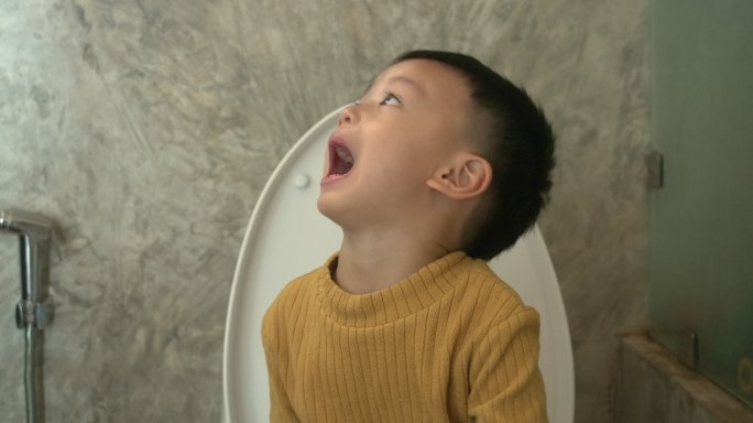 可爱的亚洲男婴坐在家里的马桶上