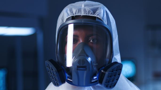 一位身穿防护服、戴着现代防毒面具的非洲裔美国年轻女性，站在现代实验室的背景下，转向镜头，看着镜头