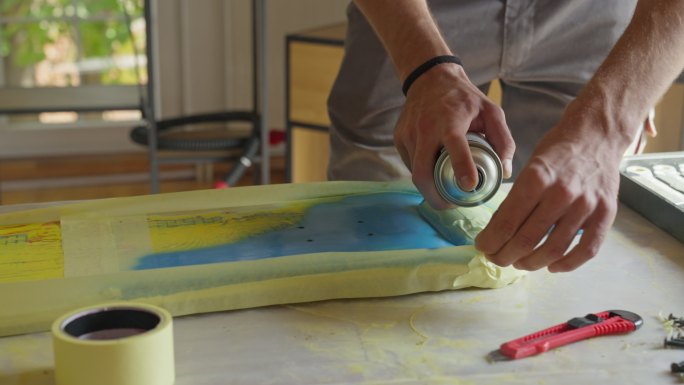 白人男性手工艺人的B卷，用喷漆在他的车间里给滑板表面喷漆