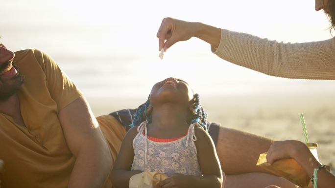 在阳光明媚的夏季海滩上，顽皮的妈妈正在喂可爱的蹒跚学步的女儿