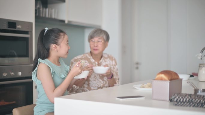 亚洲华裔老太太和孙女在厨房柜台吃中国饺子