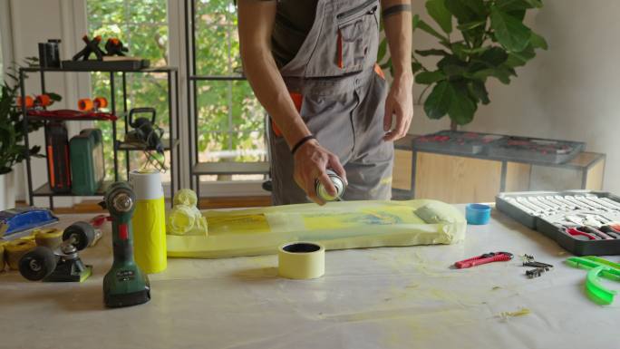 白人男性手工艺人，用喷漆在他的工作室里为滑板表面喷漆