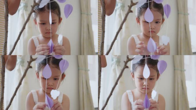 一个亚洲小女孩在复活节假期帮助父母用挂在树枝上的花环装饰房间。