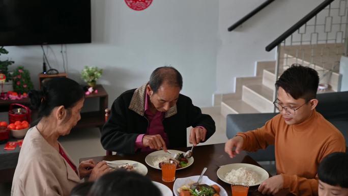 中国春节期间，一名亚洲男子在家里吃团圆饭时与母亲分享食物