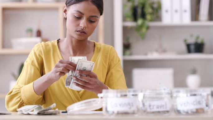 一个年轻女人在罐子里存钱。一个年轻的女人在为自己的钱做预算