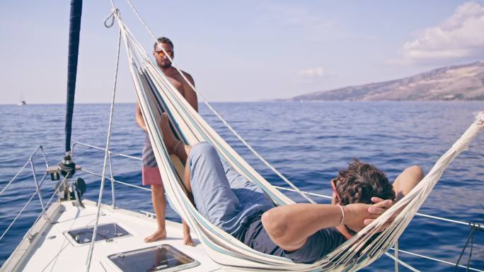 男人在吊床上放松，在阳光明媚的帆船上与朋友聊天，实时