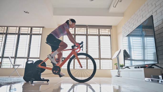亚洲中国女子在家与固定自行车教练一起骑车