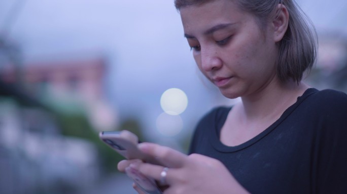 亚洲女性晚上使用智能手机在线文本聊天。