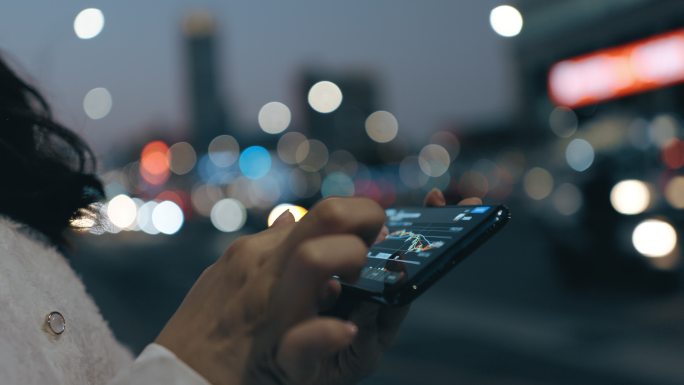 夜晚灯光模糊的城市街道上，女性手持手机上网的特写。