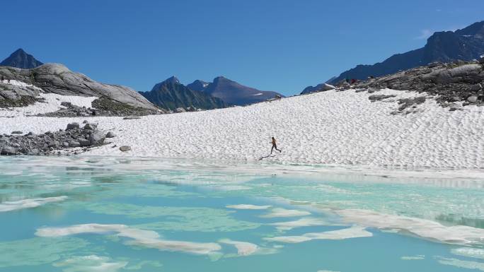 鸟瞰陡峭的山峰和覆盖着浮冰的绿松石湖。探索极端地形的女人
