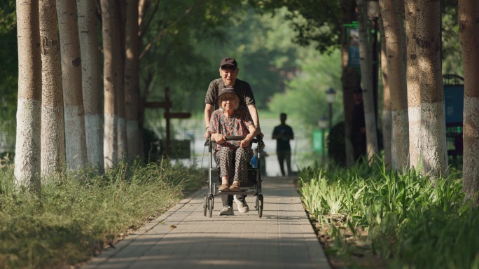 老人丈夫推着坐在轮椅上的妻子在公园散步