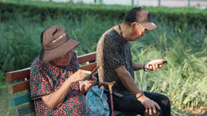 老人夫妇在公园长椅上各自看着自己的手机