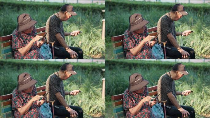 老人夫妇在公园长椅上各自看着自己的手机
