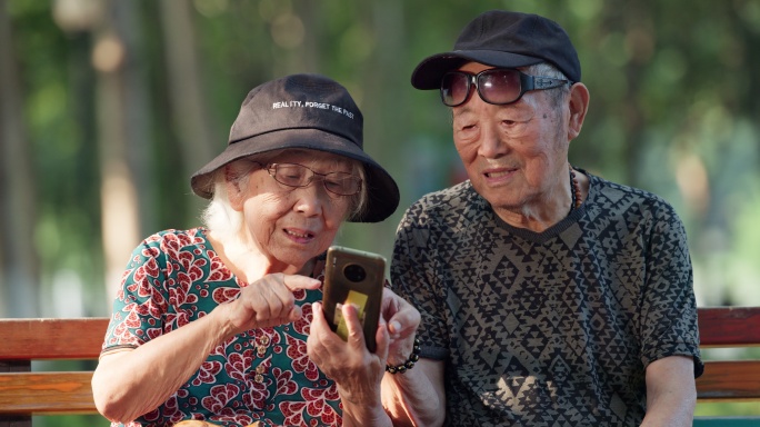 老人幸福的老年夫妇坐在公园长椅看手机聊天