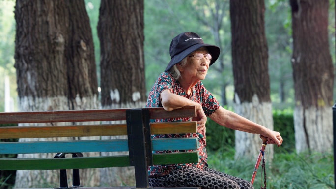 老人老年人手拄着拐棍孤独的坐在公园长椅上