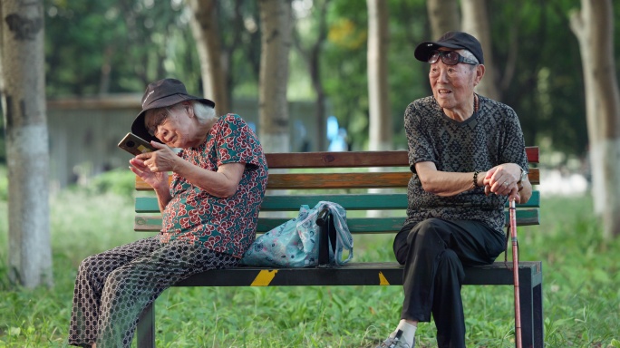老人老年夫妇在公园长椅上看手机聊天