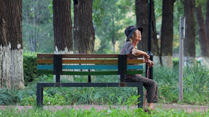 老人老年人手拄着拐棍孤独的坐在公园长椅上