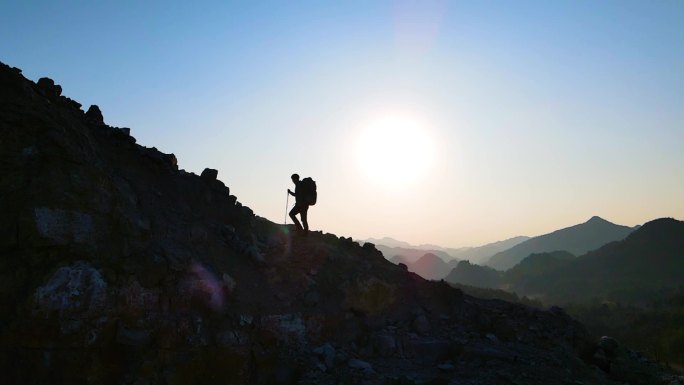 背着登山包逆光爬山人物剪影攀登顶峰成功者