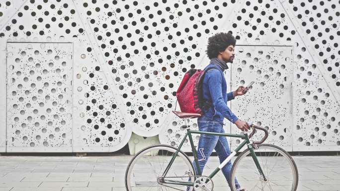 嬉皮士骑着自行车用手机在街上行走的慢动作视频