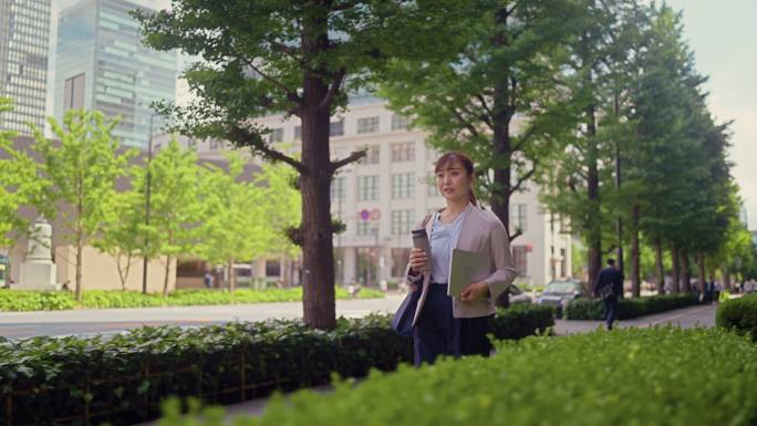 女商人拿着笔记本电脑和可重复使用的水瓶走在城市的街道上