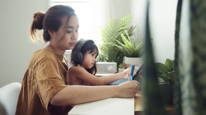 亚洲女儿和母亲一起在家上网课。