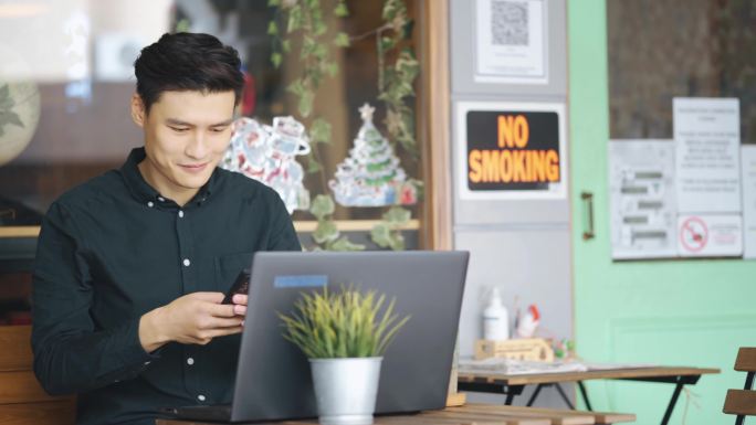 面带微笑的年轻亚洲中国商人在户外咖啡馆用笔记本电脑工作