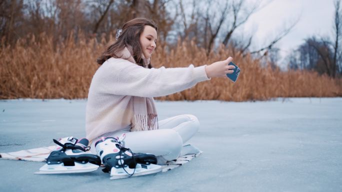 年轻女子坐在冰冻的湖面上用手机自拍