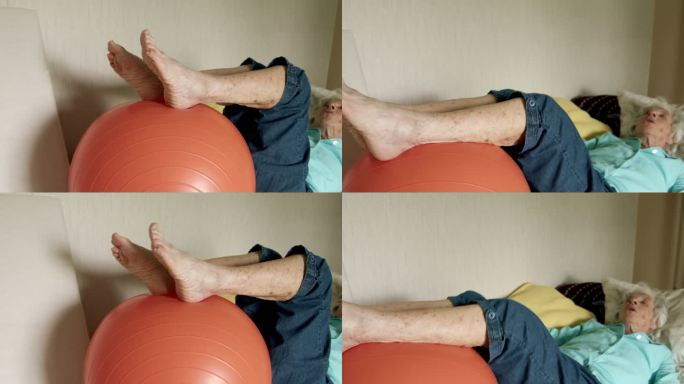 老年高加索妇女躺在床上用健身球进行日常锻炼，以保持健康、灵活和强壮