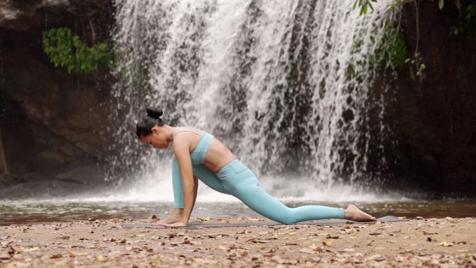 快乐女人瑜伽姿势在自然瀑布背景下平衡身体冥想。