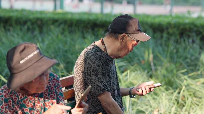 老人老年夫妇在公园长椅上看手机