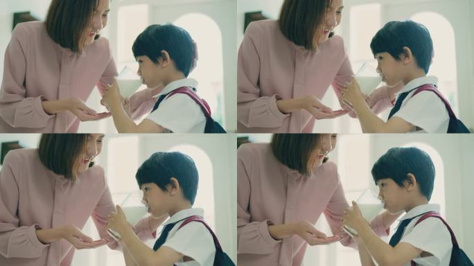 美丽的亚洲母亲鼓励她穿着校服、背着双肩包的小儿子在早上上学前喝鲜奶，以保持孩子健康的生活方式。小男孩