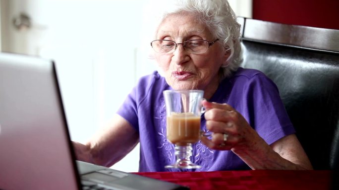 老年妇女使用笔记本电脑和喝茶