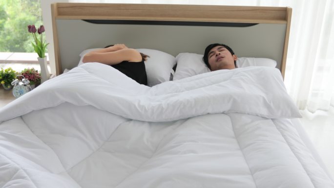 亚洲年轻妻子睡不着觉，丈夫在她身边打鼾，女人用枕头捂住耳朵。
