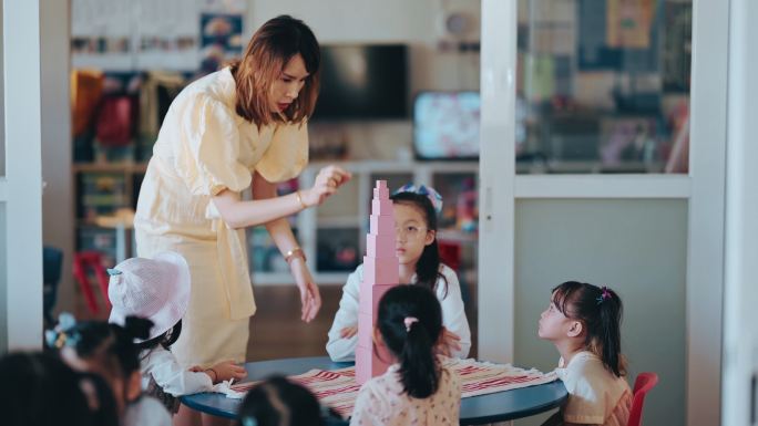 亚洲华人蒙台梭利幼师在教室里展示学生用玩具积木搭建塔