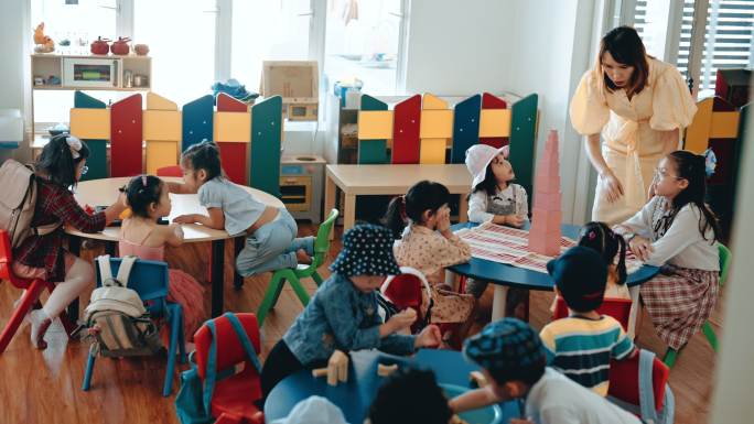 亚洲华人蒙台梭利幼师在教室里展示学生用玩具积木搭建塔
