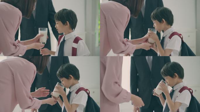 欢迎上学后回家，美丽的亚洲母亲正等着她的小儿子从学校回来，手里拿着一杯牛奶。小学小男孩放学后正在喝鲜