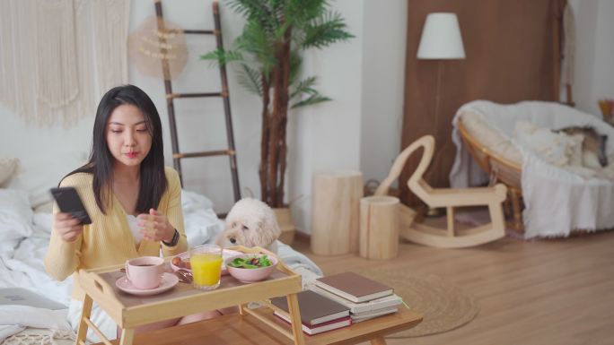周末早晨，亚洲中国美女在床上与玩具贵宾犬一起享用早餐