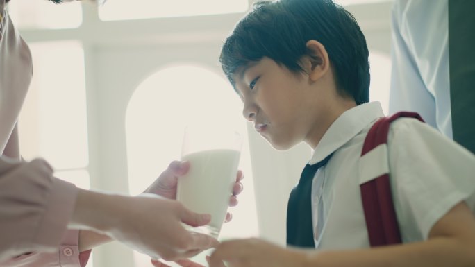 是时候喝杯牛奶了，孩子们上学前要健康饮食。快乐可爱的男孩早上喝着妈妈给的鲜奶。为幼儿提供健康均衡的营