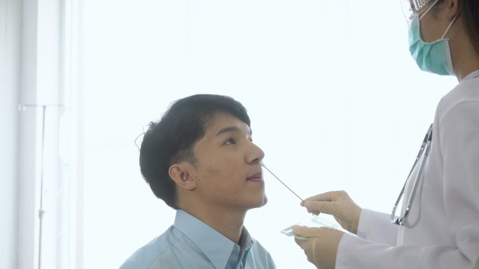 穿着防护服的专业卫生保健医生在进行冠状病毒感染时从年轻女性鼻子鼻培养物采样中取鼻拭子的侧视图19