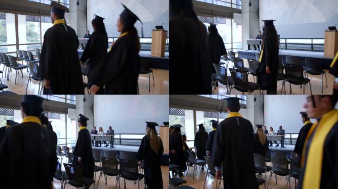 一群学生走进他们的毕业典礼，而董事会成员坐在桌子旁边，手里拿着所有的毕业证书