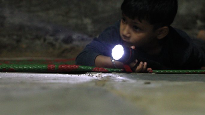 小男孩拿着手电筒在黑暗中寻找。