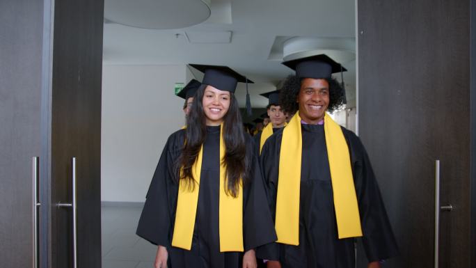 一群快乐的学生穿着莫塔巴德和毕业礼服，面带微笑地走进他们的毕业典礼