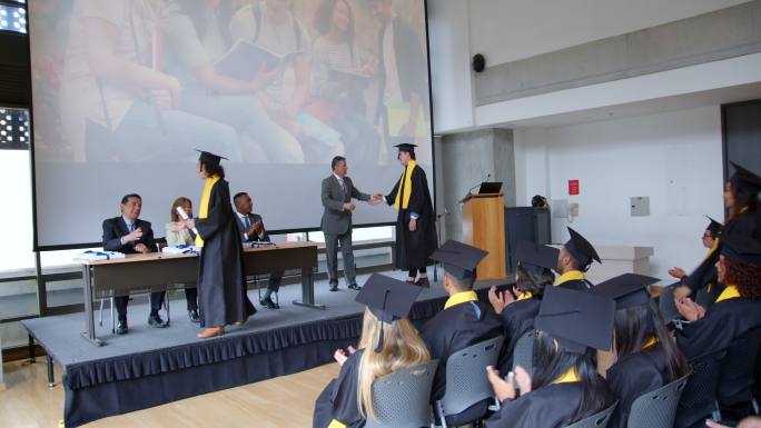 一群收到毕业证书的学生与董事会成员握手，而同学们则兴高采烈地鼓掌