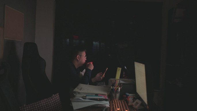 中国中年男性深夜独自在家工作，在黑暗中对着台式电脑，使用多屏幕