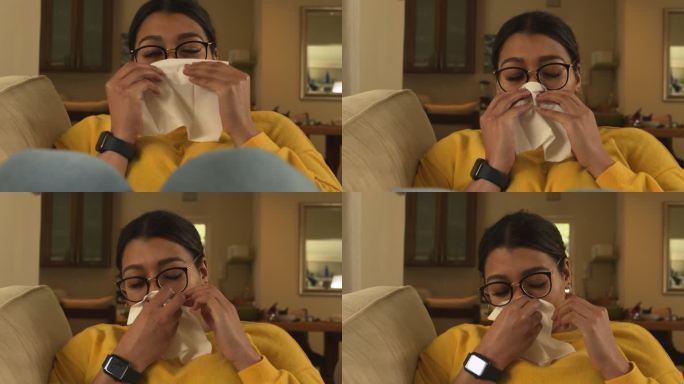 一名年轻女子在家中的沙发上擤鼻涕，正在养病。在休息室的沙发上使用纸巾并感到恶心的女人